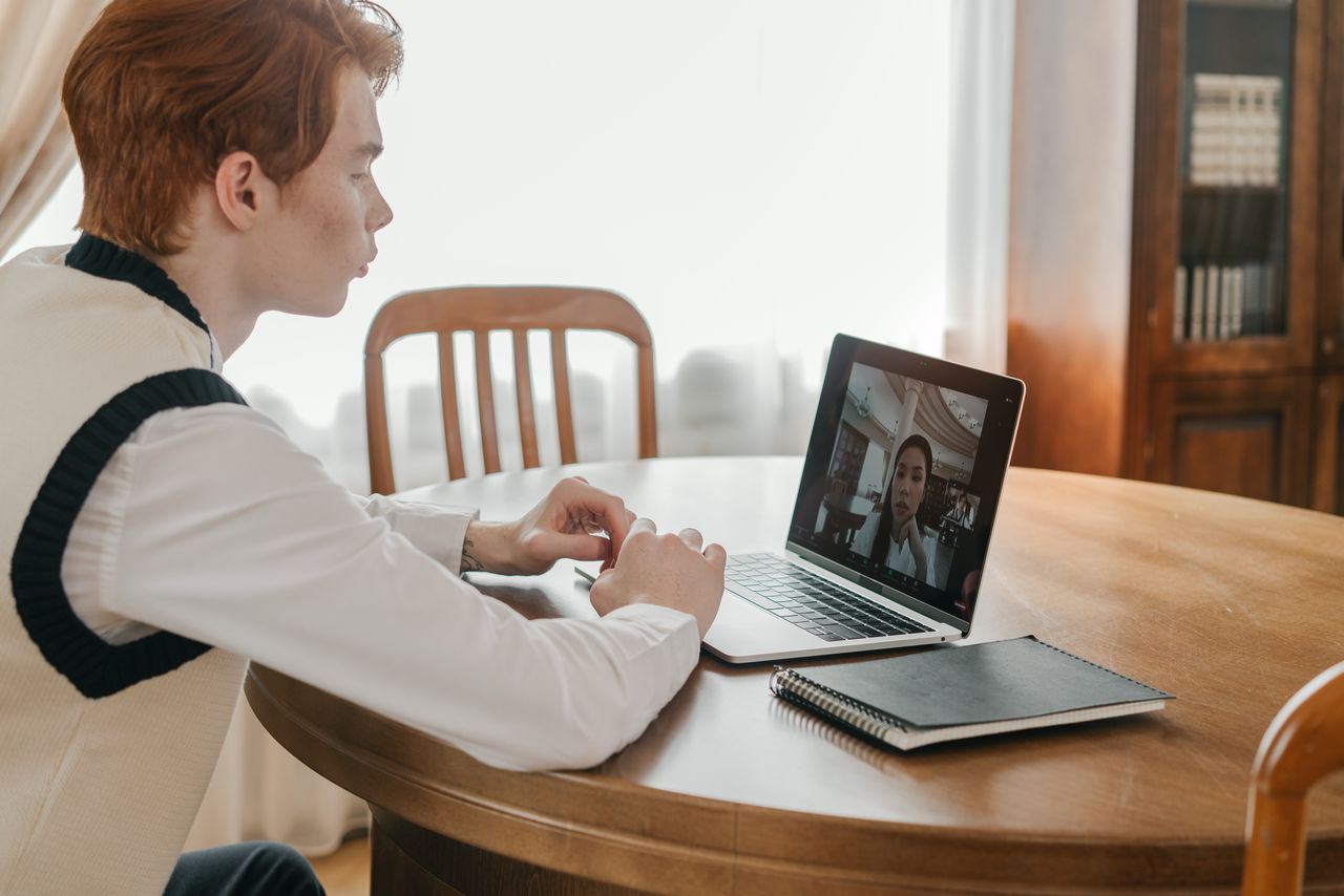 Young man involved in a video call on a laptop at home, showing remote communication.